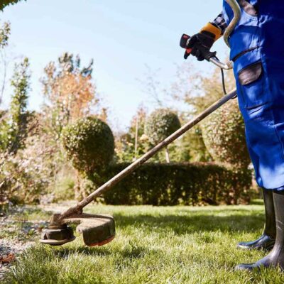 Gardener with weedwacker cutting the grass in the garden